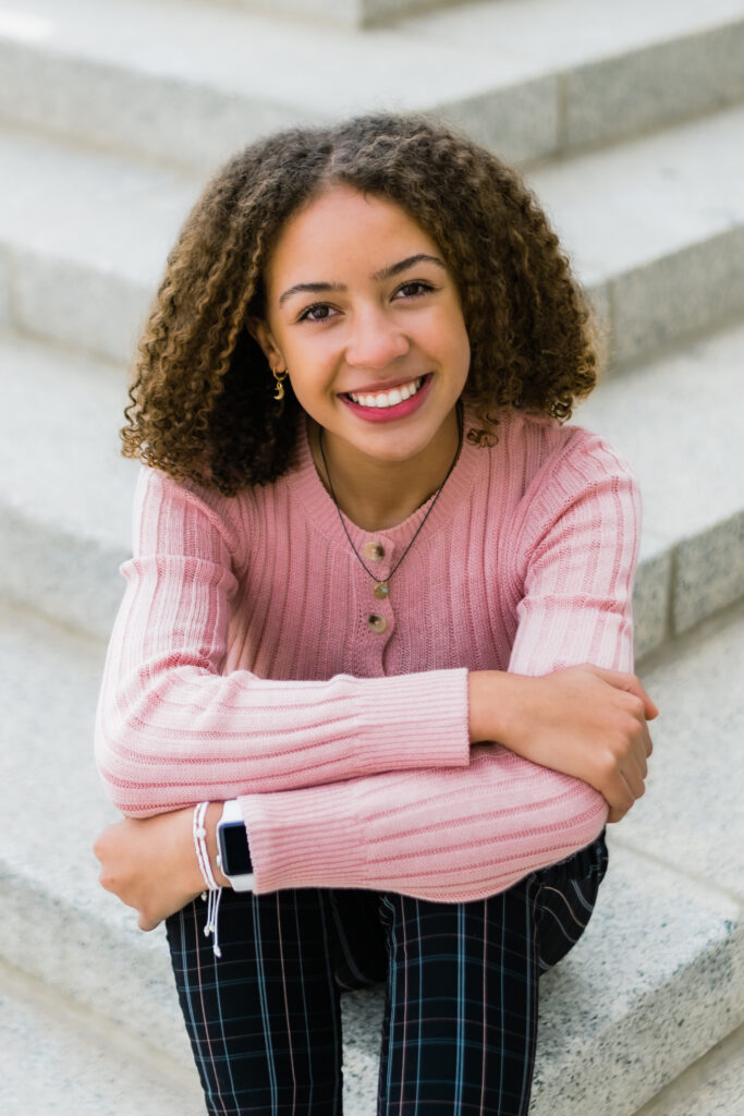 Stylish teen with curly hair smiling on the stairs after receiving orthodontic treatment.