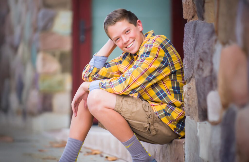 Young man smiling while sitting on a doorstep in a yellow plaid shirt on a fall afternoon