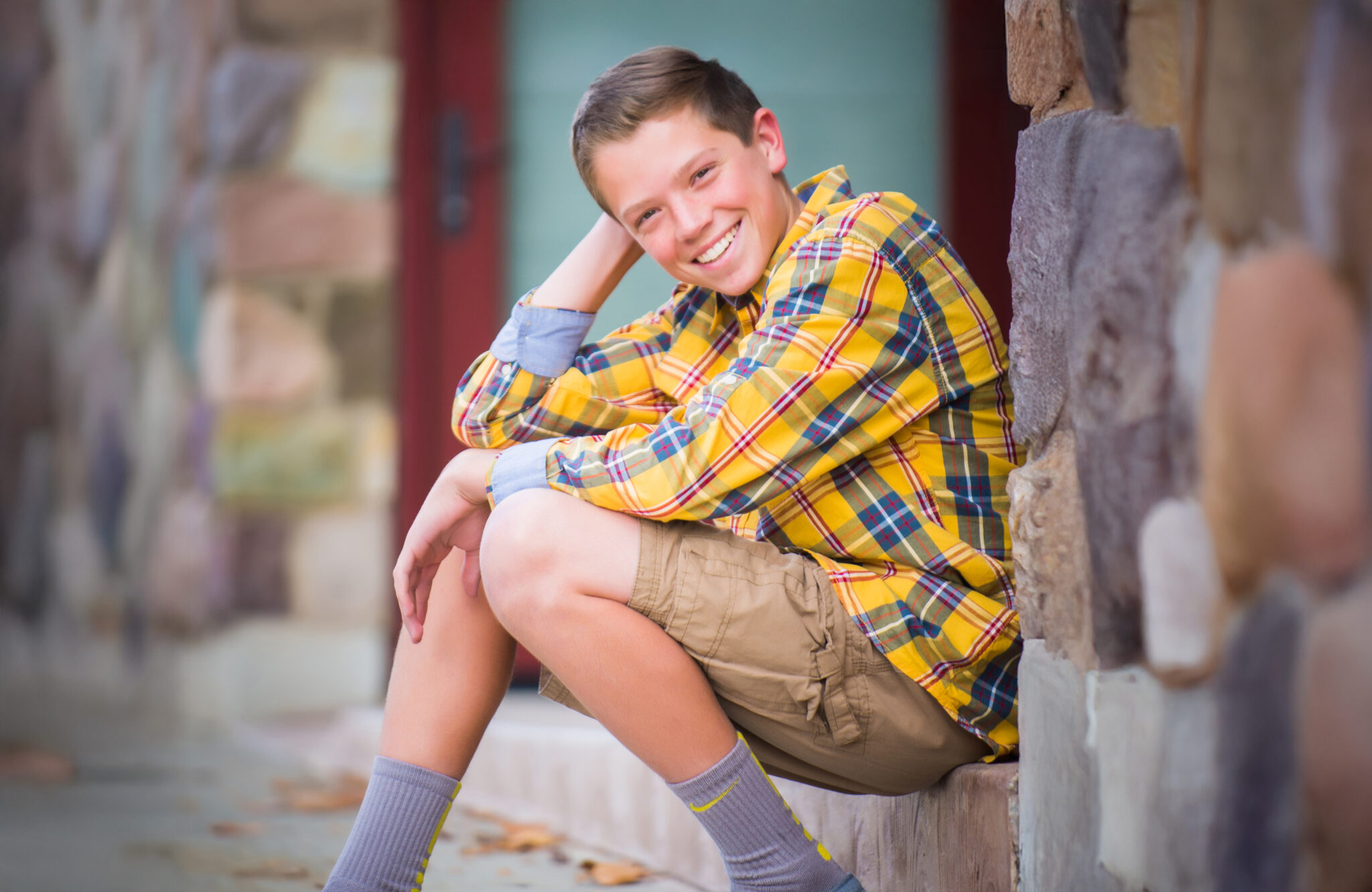 Young man smiling while sitting on a doorstep in a yellow plaid shirt on a fall afternoon