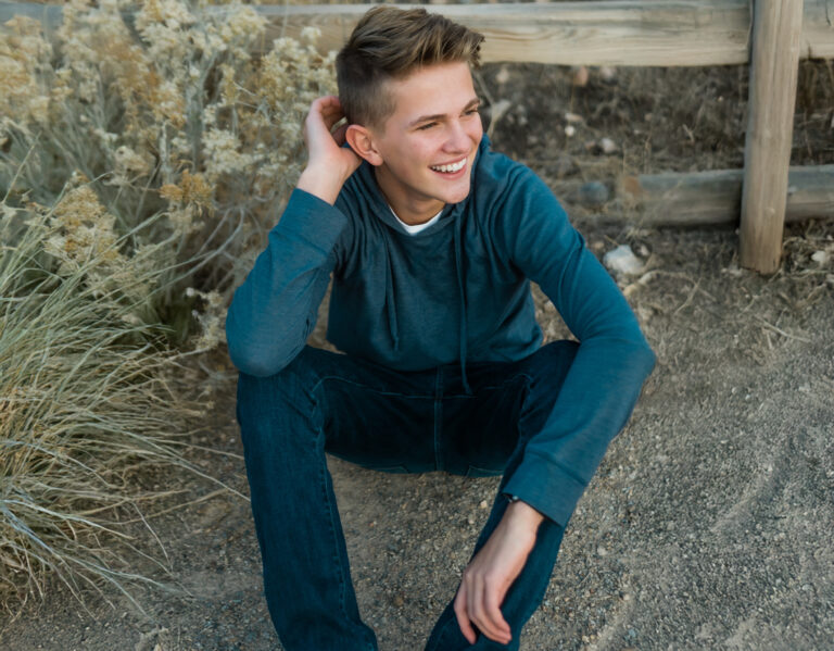 Teen sitting by a wooden fence in a cerulean hoodie and blue jeans