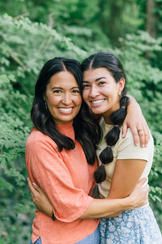 Mother and daughter embracing outside in front of lush green foliage
