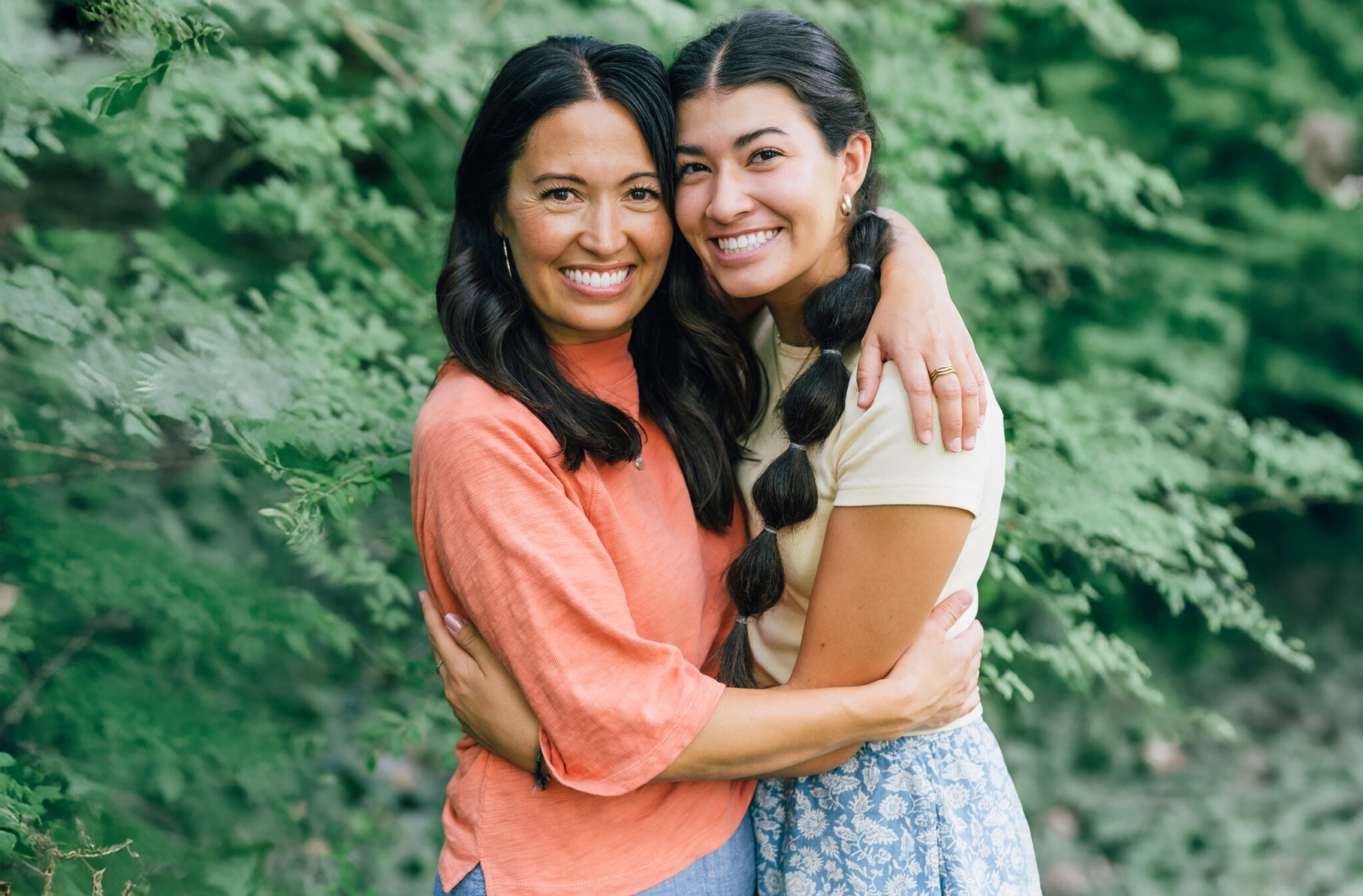Mother and daughter embracing outside in front of lush green foliage