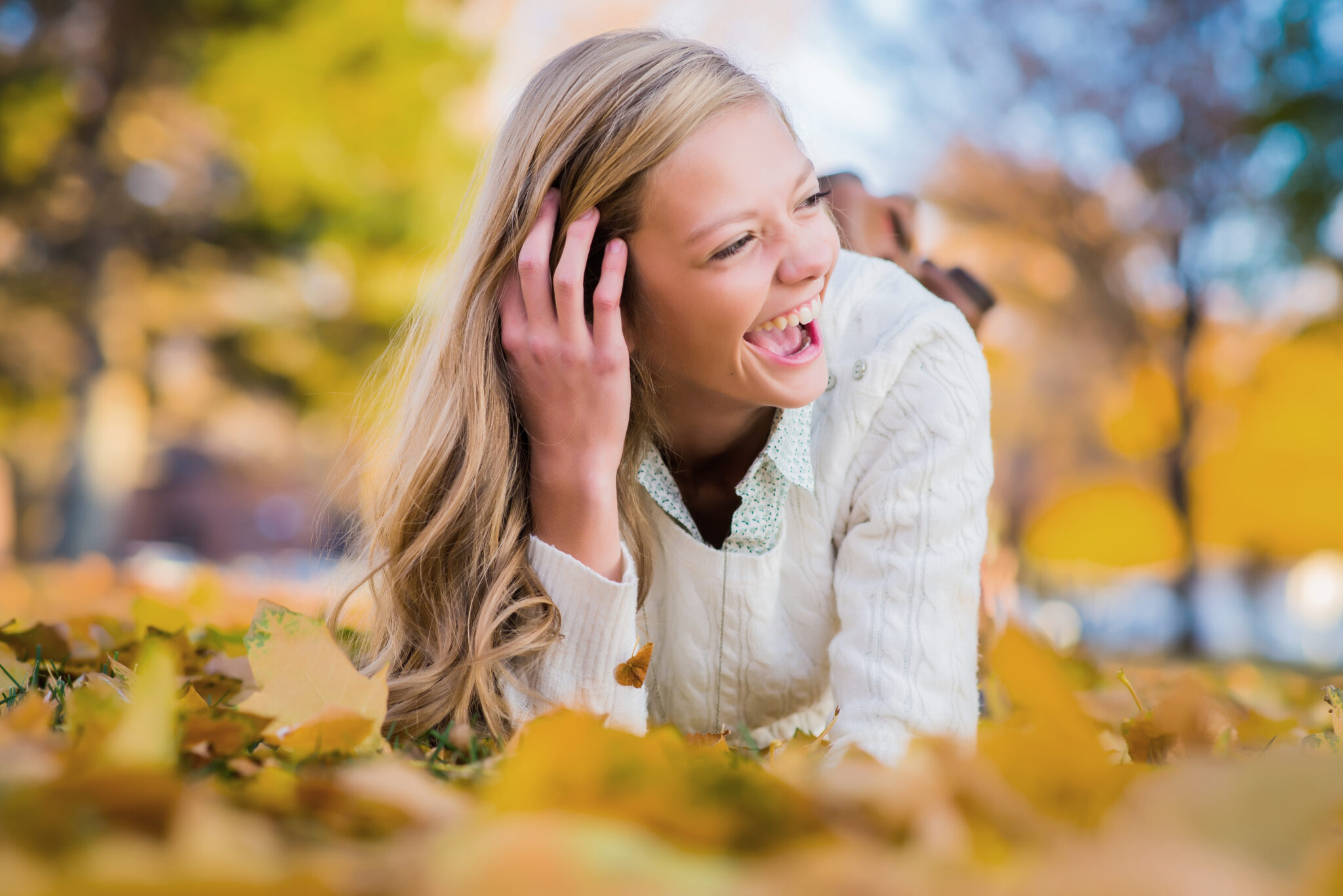 Young lady laughing while laying in the autumn leaves and running her fingers through her hair